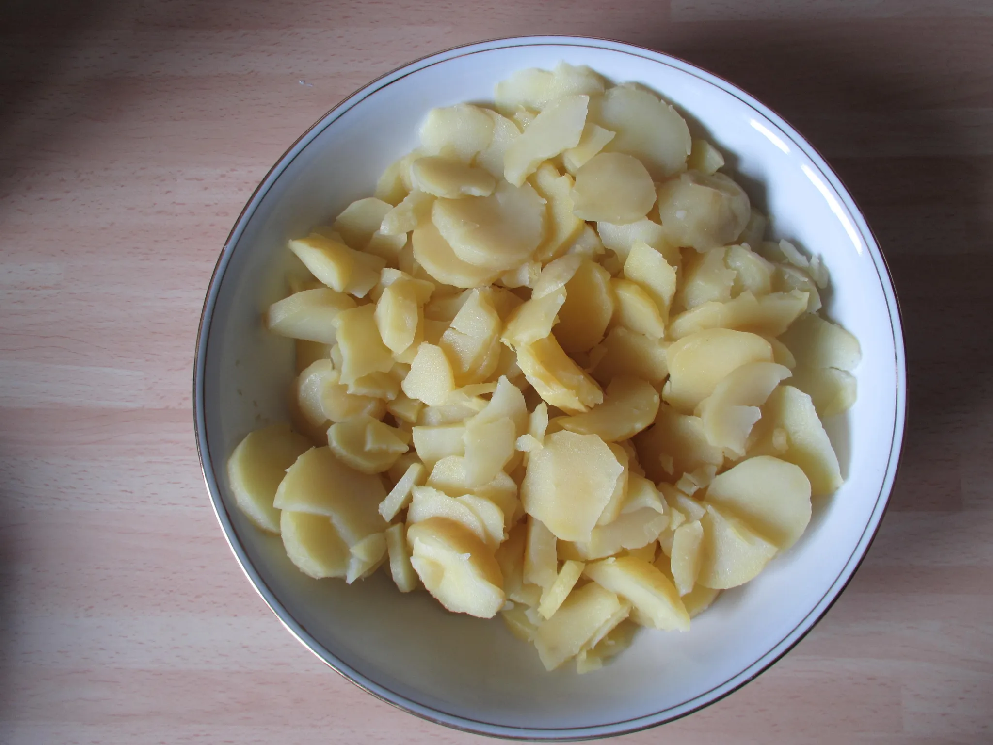 Kartoffeln als Pellkartoffeln ca. 30 Minuten in einem Topf mit Wasser gar kochen. Danach kurz abkühlen lassen, abpellen und in Scheiben schneiden.